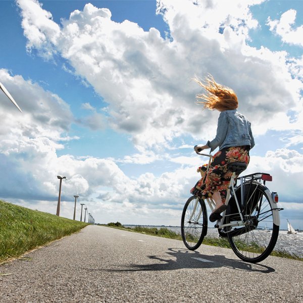 Young woman cycles on a windy road in the Netherlands, wind turbines in the background