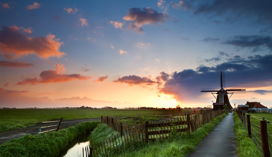 Colored Dutch sky with clouds behind windmill in typical Dutch landscape