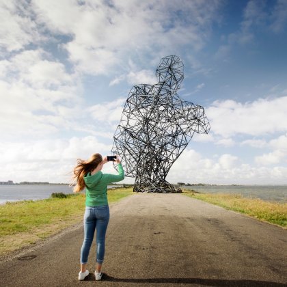 Lady takes photo of Land Art Flevoland Antony Gormley's Exposure (also called: the squatting man)