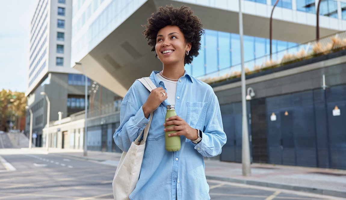 Happy curly haired woman carried fabric bag holds fresh water in bottle