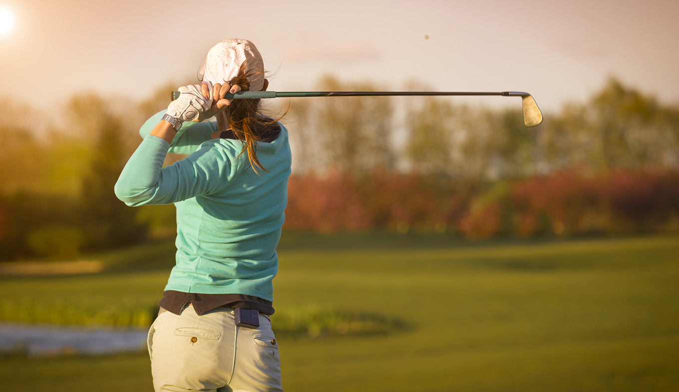 Female golfer swinging golf club on fairway during sunset