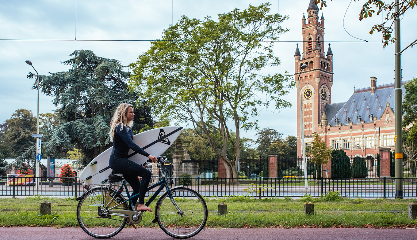 Women with a surfboard riding on a bike The Hague