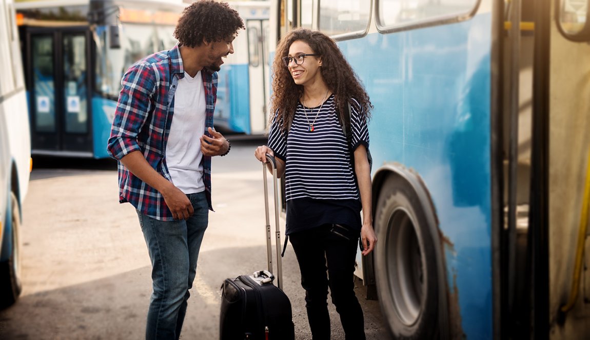 Young happy couple standing and talking in front of the bus with their suitcase